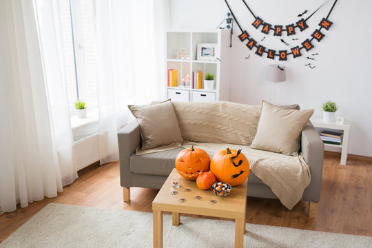 Holidays, Decoration And Party Concept - Home Room With Jack-o-lantern Or Carved Pumpkin, Halloween Decorations And Treats On Wooden Table