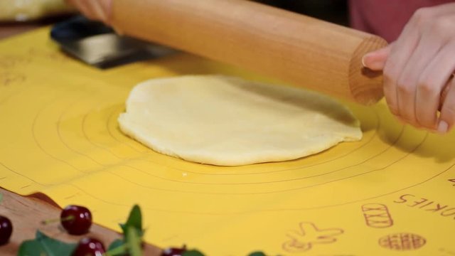 Woman hands roll out the dough on the kitchen table to make a pie with berries.