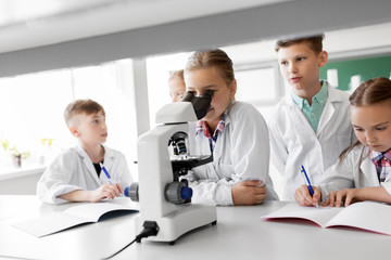 Obraz premium education, science and children concept - kids or students with microscope studying biology at school laboratory