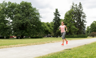 fitness, sport and healthy lifestyle concept - smiling woman with earphones running at park and...