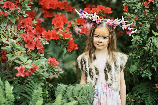 Fairy tale girl. Portrait a little girl in a deer dress with a painted face in the forest. Big antler. Fantasy girl. Springtime.