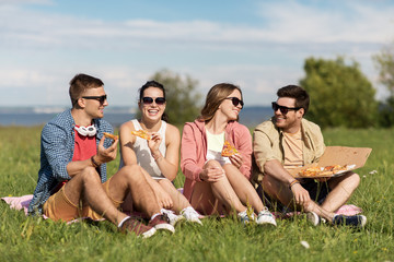 friendship, leisure and food concept - group of smiling friends eating pizza at picnic in summer...