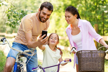 family, leisure and technology concept - happy mother, father and little daughter with smartphone...