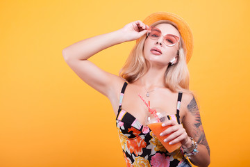 Naklejka premium happy young blonde woman holding fresh orange juice in studio