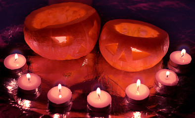 Two orange glowing carved pumpkin heads for the holiday of Helloon, surrounded by seven candles,...