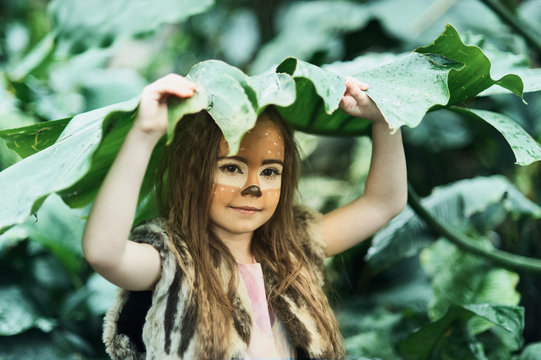Fairy tale girl. Portrait a little girl in a deer dress with a painted face in the forest. Big antler. Fantasy girl. Springtime.