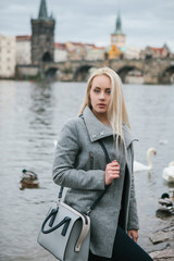 Fashionable blonde with long hair in a coat near Charles Bridge in Prague. Beautiful young woman outdoors.