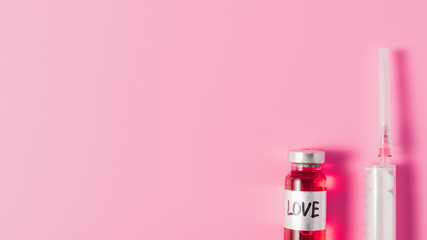 top view of syringe and bottle with love vaccine sign on pink tabletop