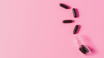 top view of black medical capsules spilled from bottle on pink