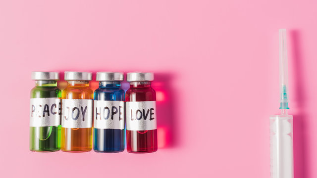 Top View Of Syringe And Bottles With Love, Hope, Joy And Peace Vaccine Signs In Row On Pink Tabletop