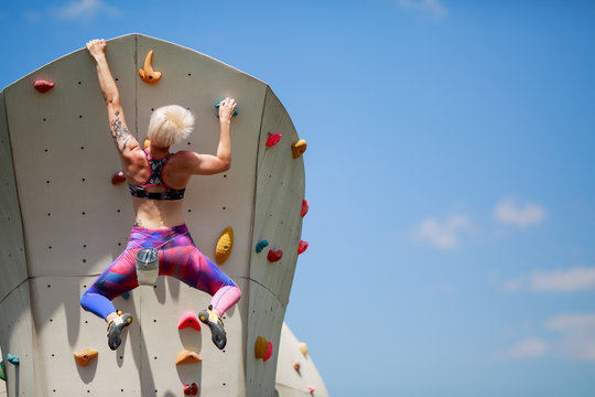 Photo from back of young athlete girl with short hairstyle climbing wall for rock against blue sky