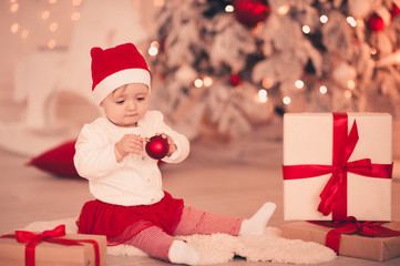Obraz na płótnie Canvas Cute baby girl wearing santa claus suit playing with christmas decorations in room over light at background. Winter season.