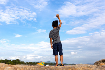 Boy raises his hands while standing on top rock looking at the sea.