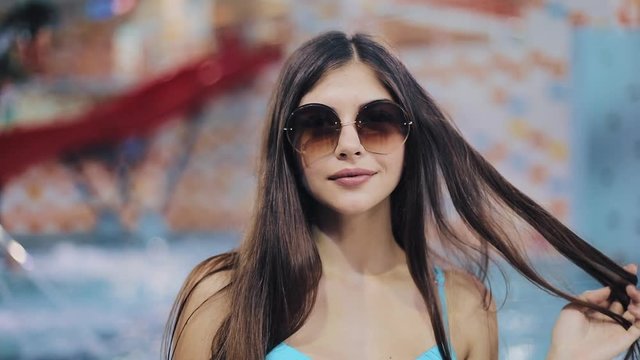 Sexy young women in blue swimsuit and sunglasses posing in pool. Portrait of an attractive girl in a water park looking at the camera