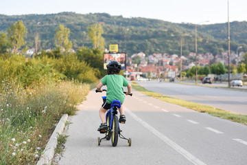 Naklejka premium Five years old boy rides a bicycle in the city. Child riding bicycle outdoor on sunny day