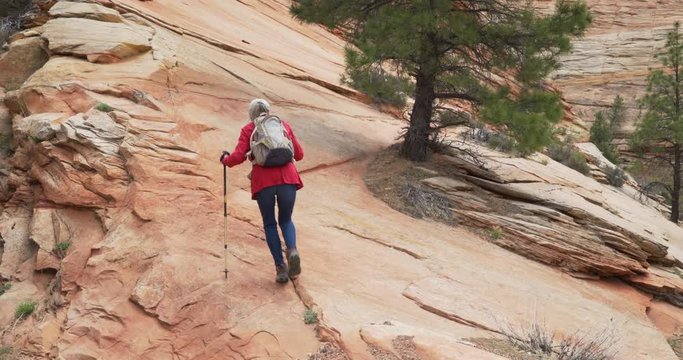 Active senior woman climbing rocky cliff with hiking staffs in Zion Utah
