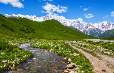 Fototapeta na wymiar Beautiful mountain stream with colorful stones. Sky with clouds. Landscape with high mountains. Eco resort, relax for tourists. Location the Upper Svaneti, Georgia, Europe.