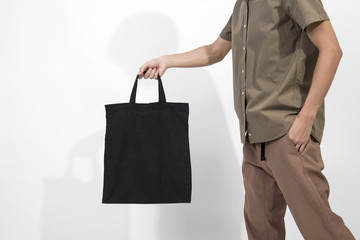 Man is holding black bag canvas fabric for mockup blank template isolated on gray background.