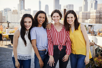 Portrait Of Female Friends Gathered On Rooftop Terrace For Party With City Skyline In Background