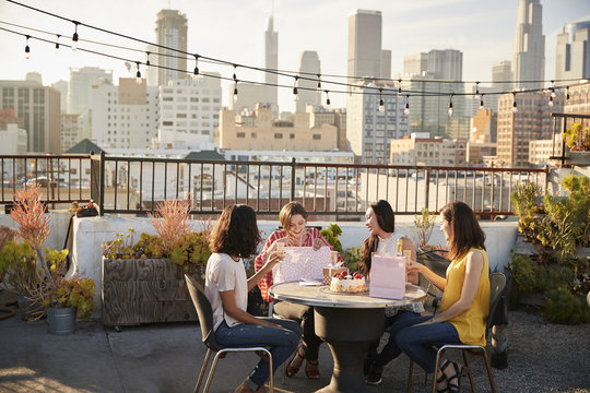 Female Friends Celebrating Birthday On Rooftop Terrace With City Skyline In Background