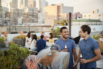 Friends Gathered On Rooftop Terrace For Barbecue With City Skyline In Background