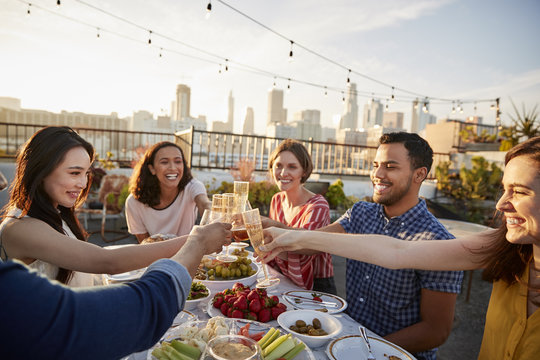 Friends Gathered On Rooftop Terrace For Meal With City Skyline In Background
