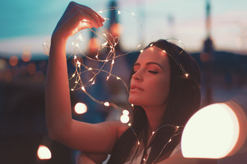Sensual woman playing with fairy lights outdoors teal and orange style