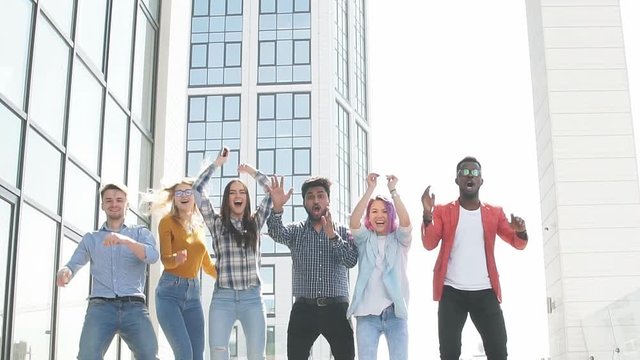 Multiracial heterosexual group of students having fun on roof party dancing and listening music at daytime on the roof area against glass office buildings background
