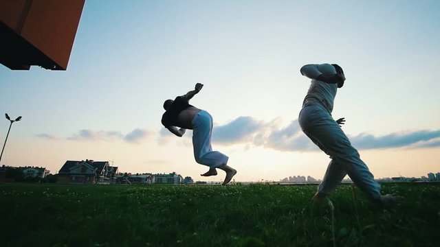 Two strong men demonstrate the art of capoeira dance on the grass