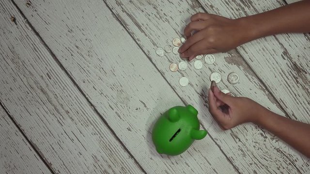 Girl's hands counting and stacking quarters on floor next to a green piggy bank.