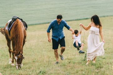 parents and son holding hands and having fun near horse on field