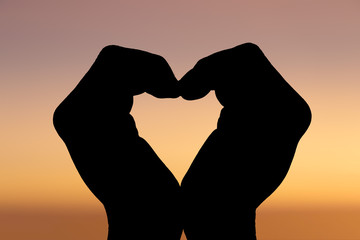 Hands of man showing heart shape with sunset in the background