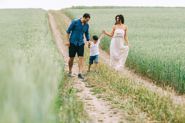 parents and son holding hands and walking on path in green field