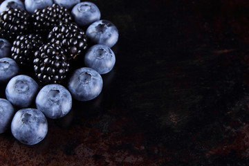 Blueberries and blackberries on dark background, fresh berries for vegan, fruits on rusty background, assorted berry breakfast
