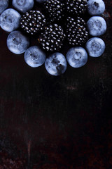 Blueberries and blackberries on dark background, fresh berries for vegan, fruits on rusty background, assorted berry breakfast