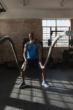 Senior man doing crossfit rope training in the fitness studio