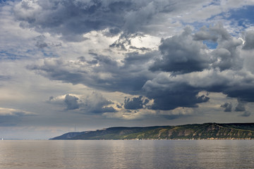 Bright beautiful clouds. The bank of the river, on the horizon of the mountain and forest. . The warm summer and the beauty of nature. Soon it will start to rain.