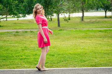 beautiful young blonde woman in a pink dress stylish high heels shoes in the summer park . concept of freshness and femininity