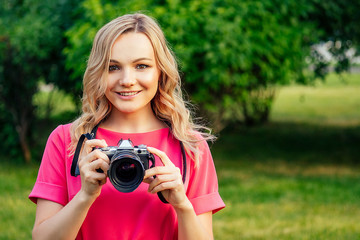 portrait of photosession professional beautiful young blonde woman in a pink dress photographed in the summer park. photographer in photoshoot with a big camera and a cool lens