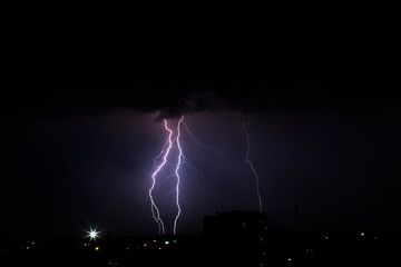 Naklejka na ściany i meble Lightning storm over city in purple light