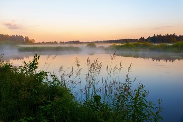 Fototapeta na wymiar Sunrise above misty landscape with pond.