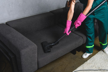 High angle view of woman in rubber gloves cleaning furniture with vacuum cleaner