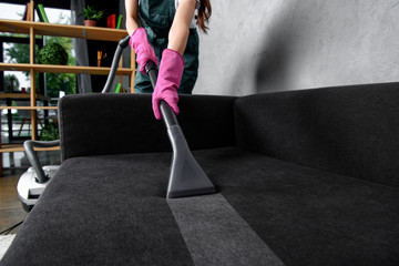 Partial view of woman in rubber gloves cleaning furniture with vacuum cleaner