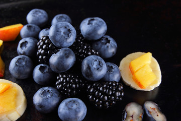 Different fruits and berries on dark background, fresh berries and pieces of banana and peach for vegan, blueberries and blackberries for breakfast