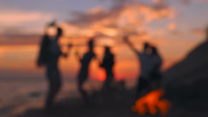 Blurred group of people having fun near the bonfire at the beach. Sunset. Slow motion.