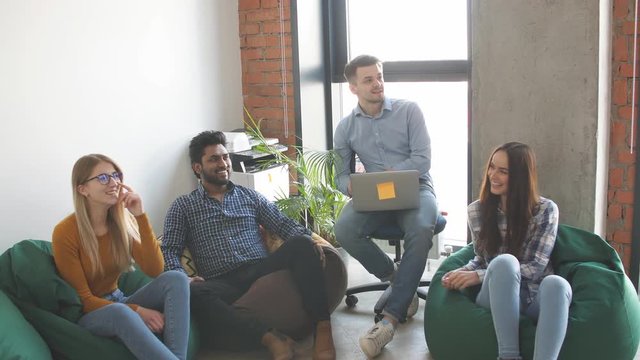 Young Indian constructor sharing new ideas about project to his partners in office working room. Multiethnic coworkers discussing over new business project in modern loft interior.
