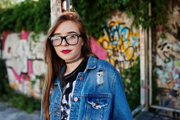 Stylish casual hipster girl in jeans wear and glasses against large graffiti wall.