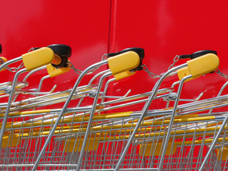 Stack of new shiny shopping carts in a supermarket with red wall in background
