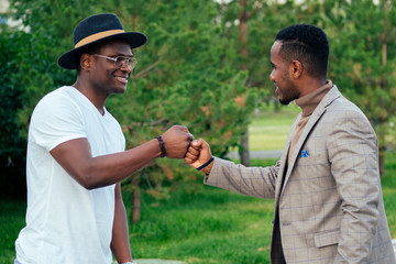 two black men in stylish suits meeting in a summer park. African-Americans friends hispanic businessman embrace hug greeting each other teamwork outdoors. successful deal concept © yurakrasil