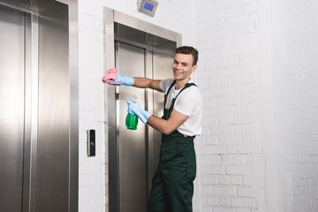Handsome young cleaner washing elevator and smiling at camera